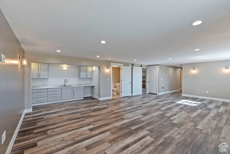 Unfurnished living room featuring dark wood-style flooring, a barn door, and recessed lighting