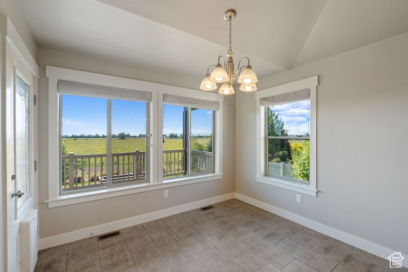 Spare room featuring plenty of natural light, a chandelier, and vaulted ceiling