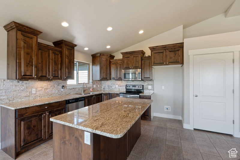 Kitchen with stainless steel appliances, decorative backsplash, a kitchen island, lofted ceiling, and light stone countertops