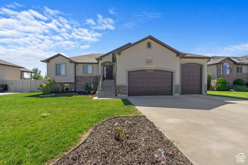 View of front facade featuring stucco siding, an attached garage, concrete driveway, and stone siding