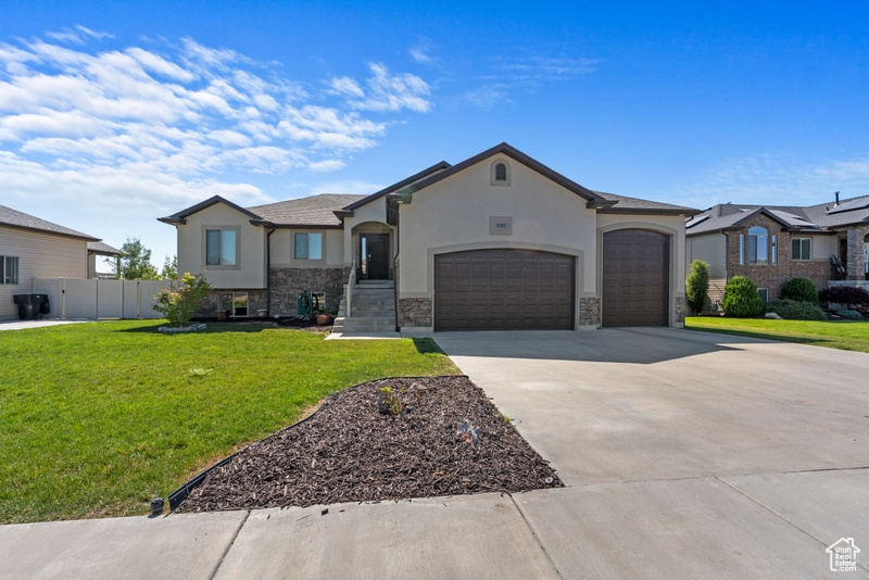 View of front facade featuring a garage, stucco siding, concrete driveway, and stone siding