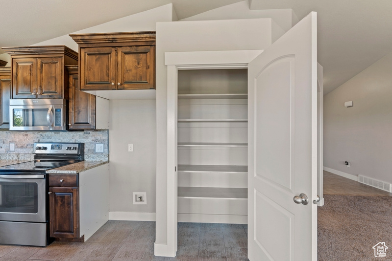 Kitchen featuring appliances with stainless steel finishes, decorative backsplash, vaulted ceiling, wood finished floors, and light stone countertops