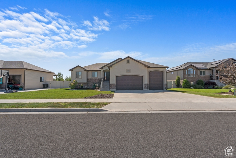 View of front of home with an attached garage, driveway, stone siding, and stucco siding