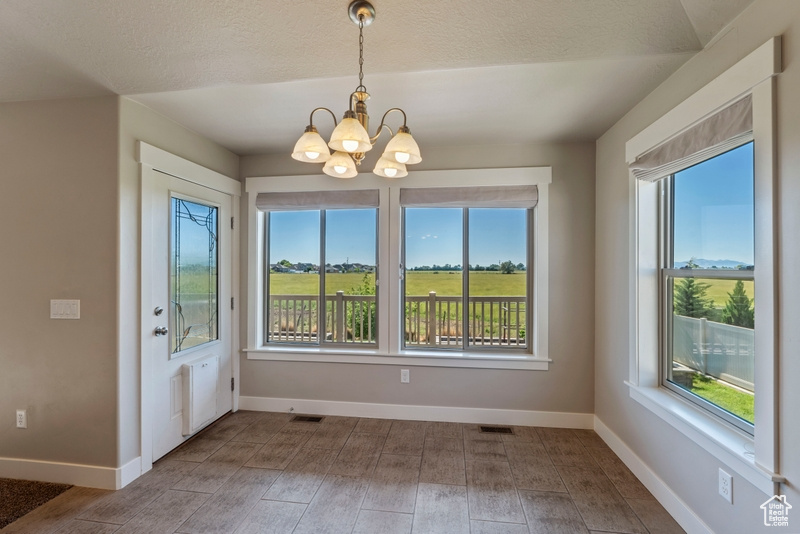 Unfurnished dining area with a chandelier, healthy amount of natural light, wood finished floors, and a textured ceiling