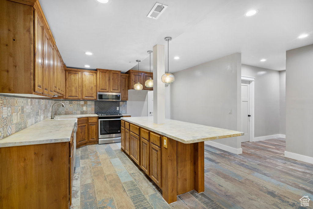 Kitchen with appliances with stainless steel finishes, brown cabinetry, light countertops, light wood finished floors, and recessed lighting