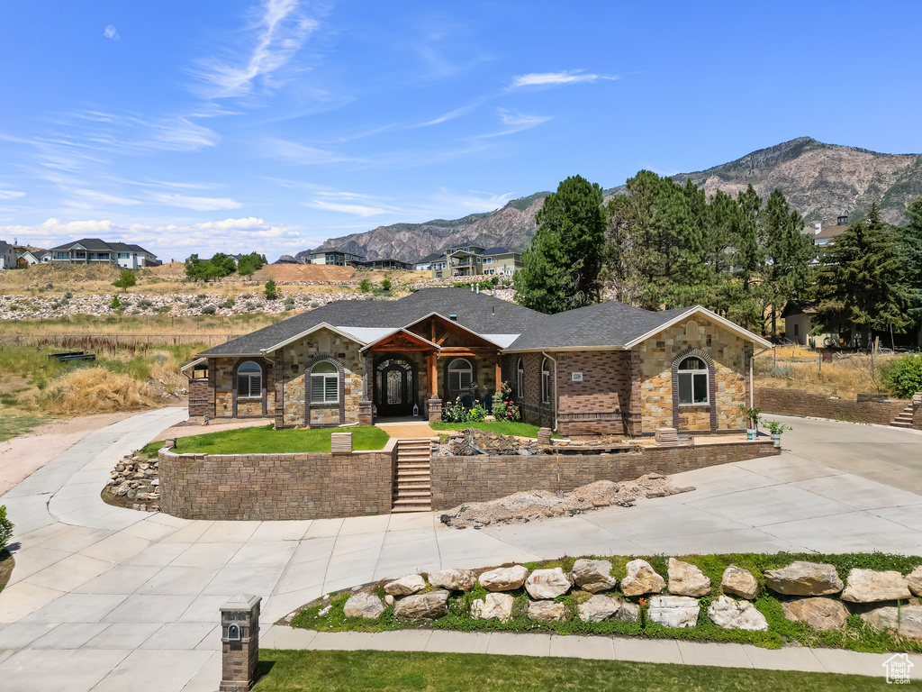 View of front facade with a mountain view, covered porch, curved driveway, brick siding, and stone siding