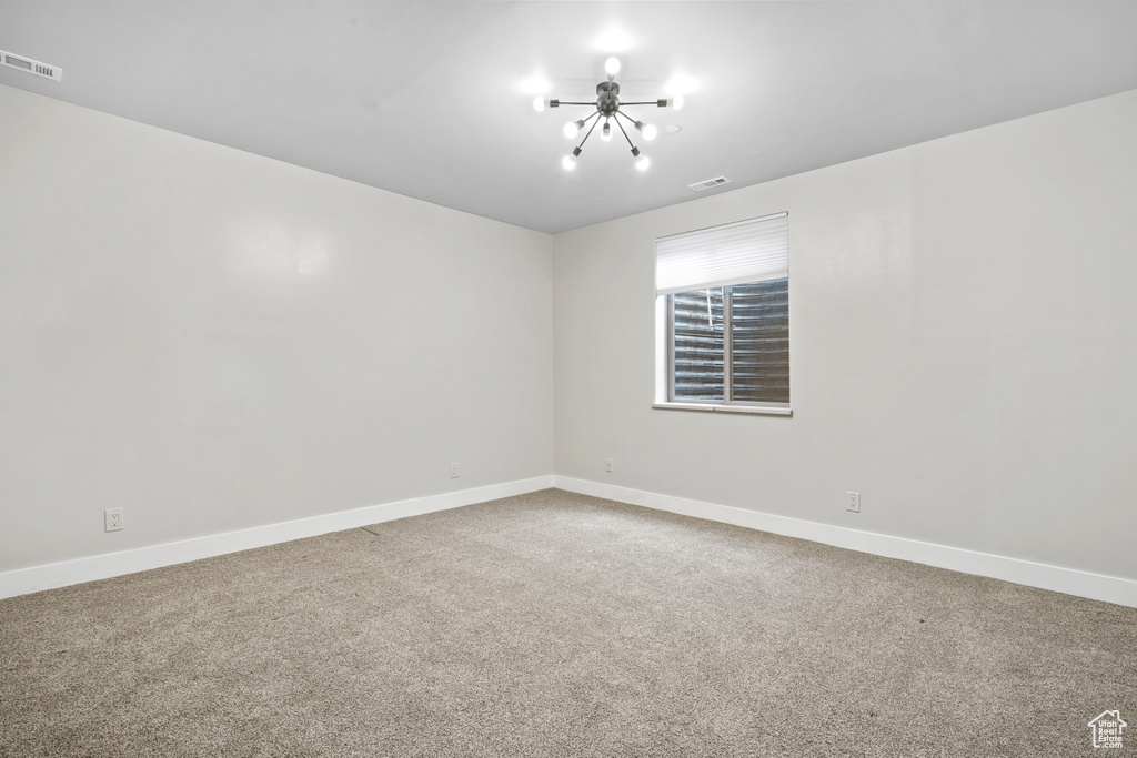 Carpeted spare room featuring a chandelier and baseboards