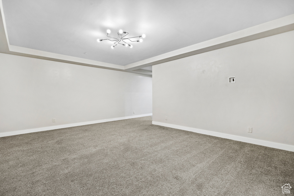 Carpeted empty room featuring a chandelier and baseboards