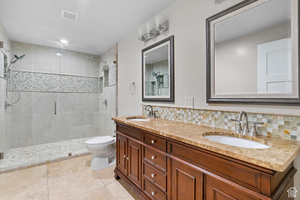 Bathroom featuring a shower stall, double vanity, tile patterned flooring, and tasteful backsplash