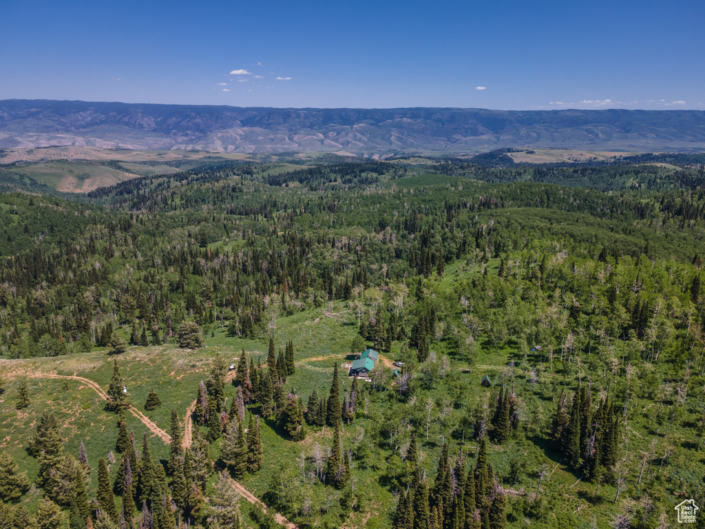 Aerial view of property and surrounding area featuring a forest and a mountainous background