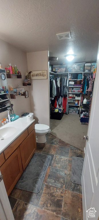 Bathroom with vanity, a textured ceiling, a walk in closet, and stone tile floors