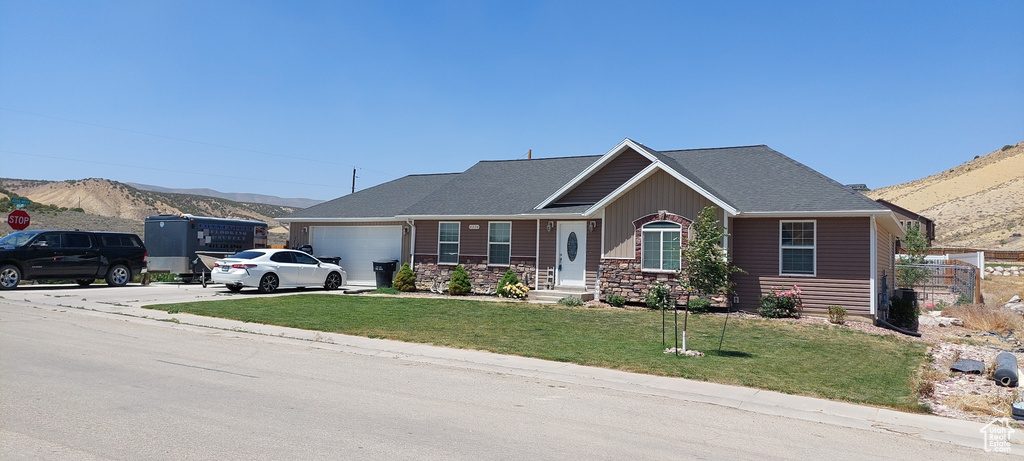View of front facade featuring an attached garage, a mountain view, driveway, a front lawn, and stone siding