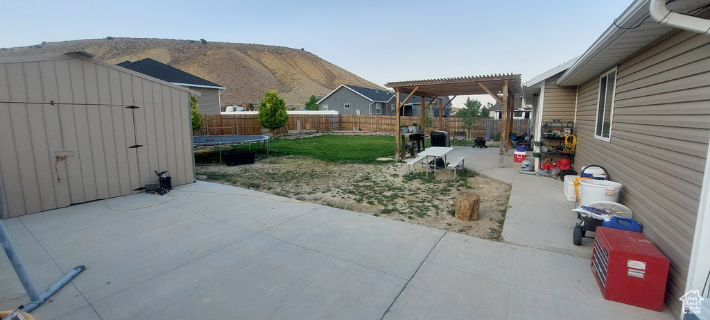 Fenced backyard featuring a patio, a trampoline, a pergola, and a shed