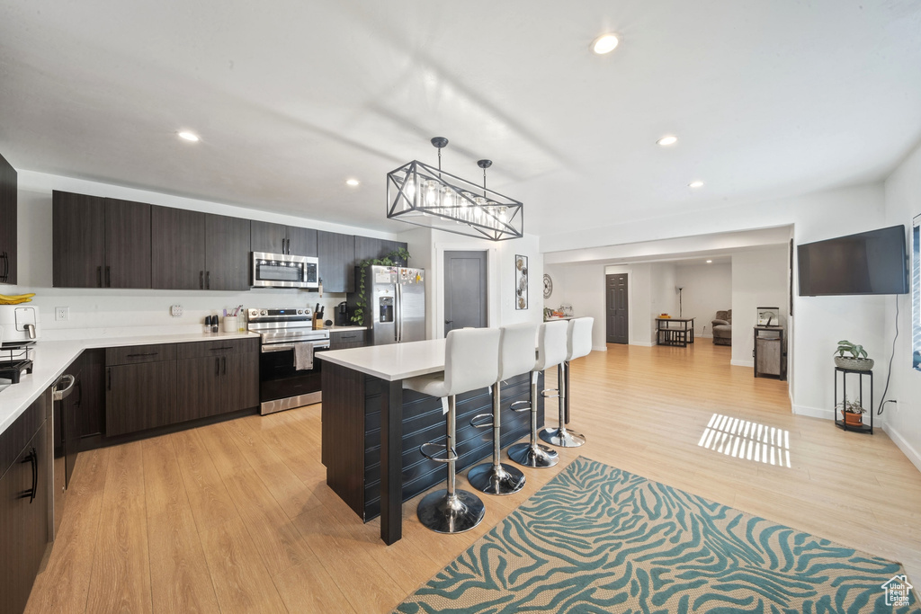 Kitchen featuring appliances with stainless steel finishes, light countertops, a breakfast bar, dark brown cabinets, and recessed lighting