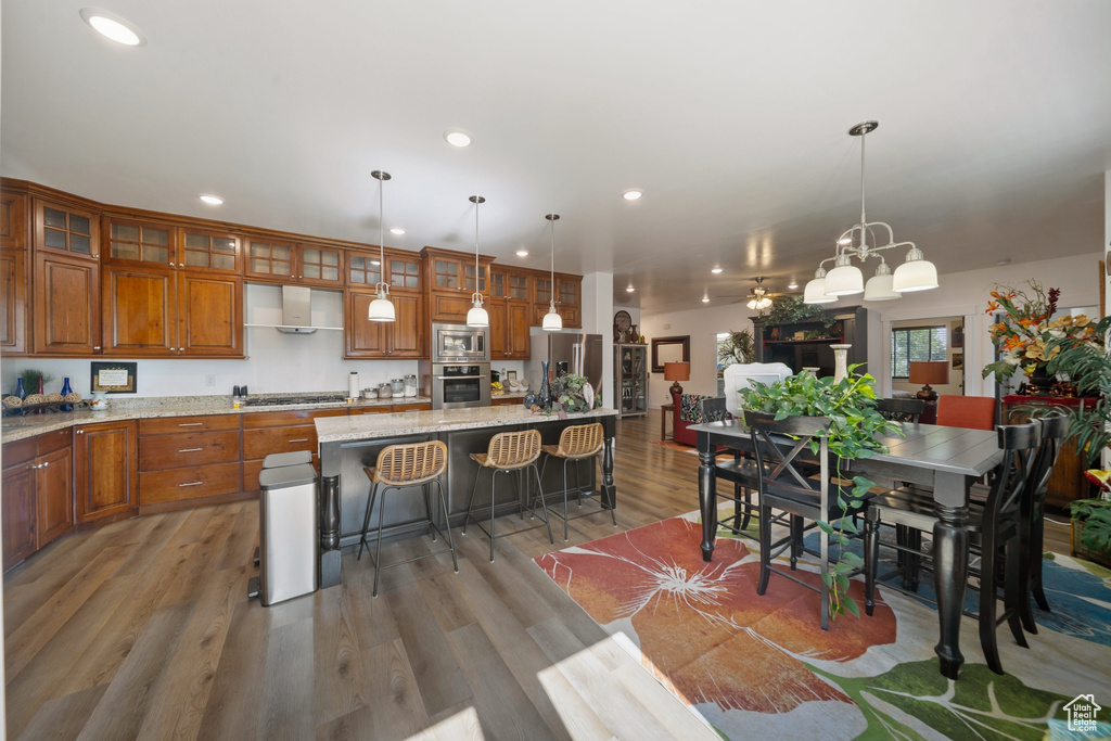 Kitchen with appliances with stainless steel finishes, brown cabinets, recessed lighting, light wood finished floors, and an island with sink