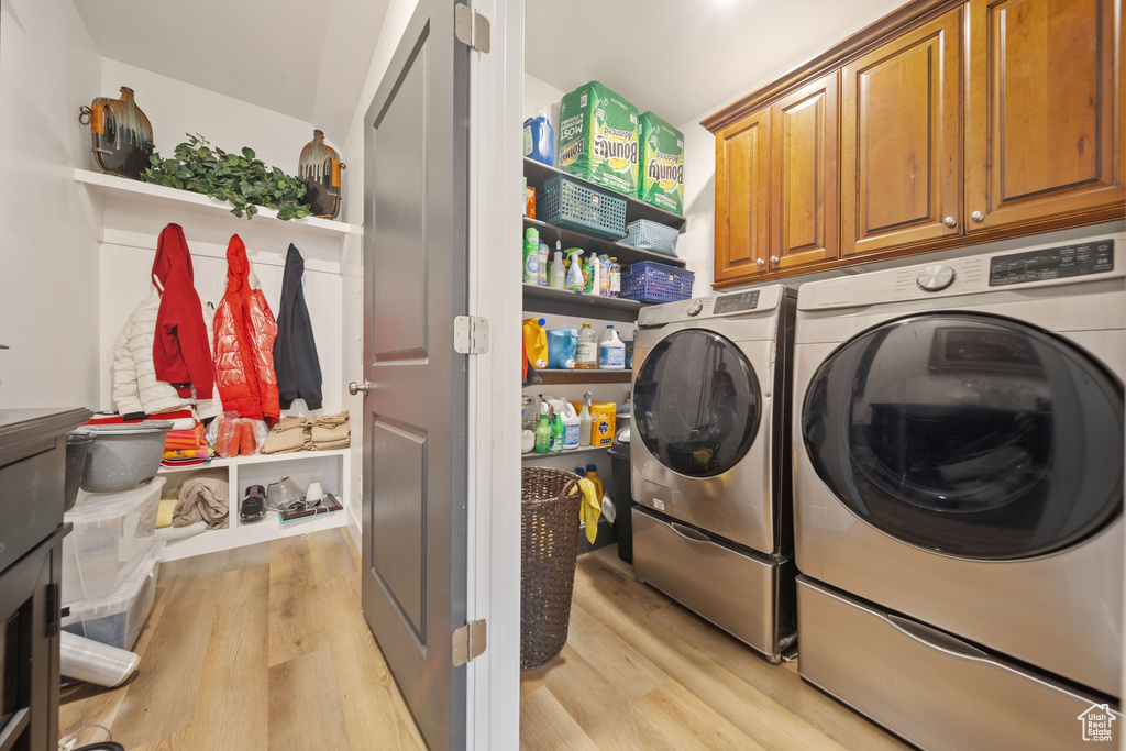 Washroom with washing machine and clothes dryer, light wood finished floors, and cabinet space