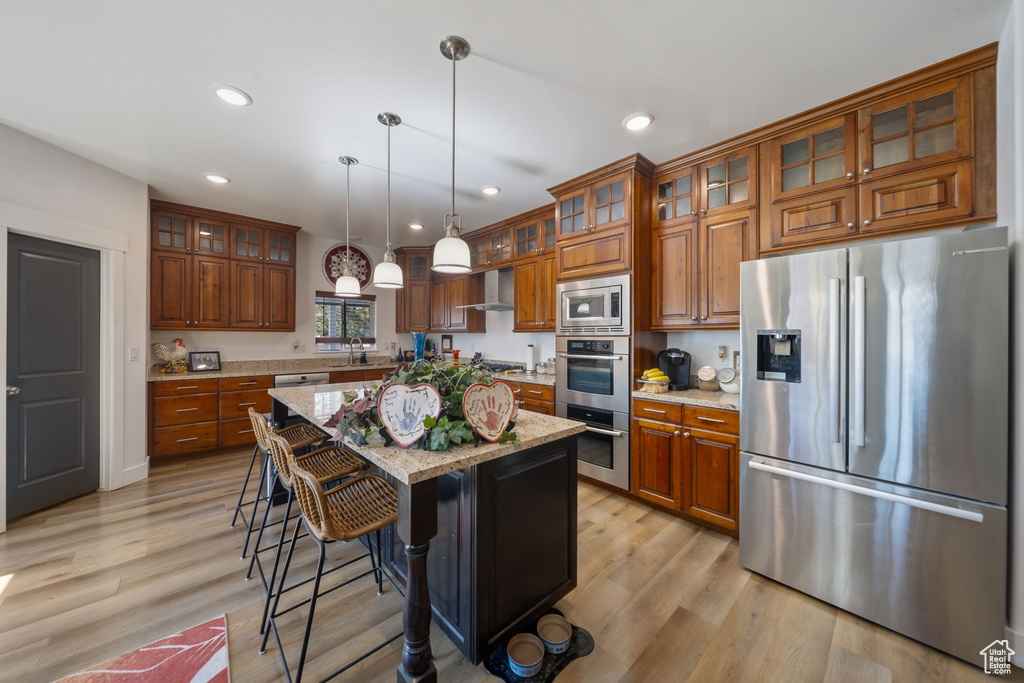 Kitchen featuring stainless steel appliances, brown cabinets, recessed lighting, a center island, and decorative light fixtures