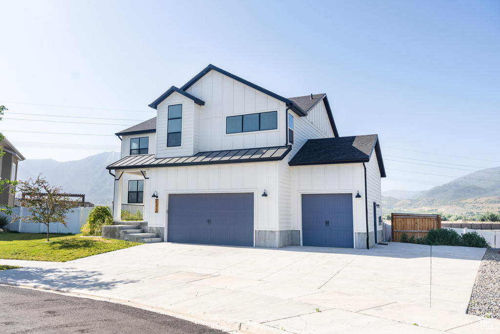 Modern inspired farmhouse featuring a standing seam roof, board and batten siding, a mountain view, concrete driveway, and a garage