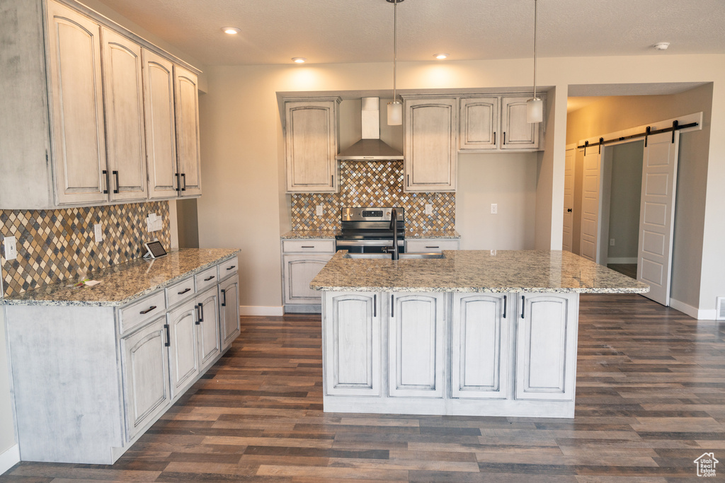 Kitchen with wall chimney range hood, electric stove, a barn door, a kitchen island with sink, and recessed lighting