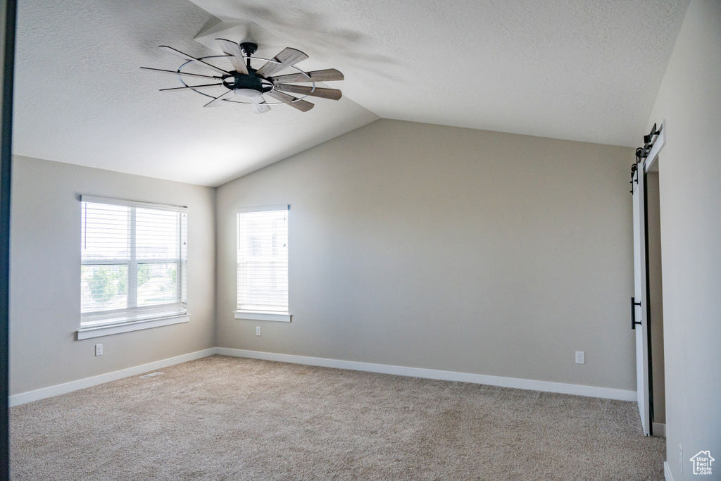 Spare room featuring vaulted ceiling, carpet flooring, a textured ceiling, a barn door, and ceiling fan