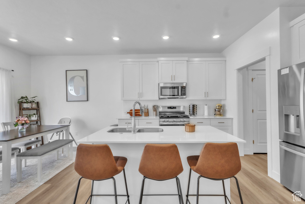 Kitchen featuring stainless steel appliances, light wood finished floors, a kitchen bar, light countertops, and a center island with sink