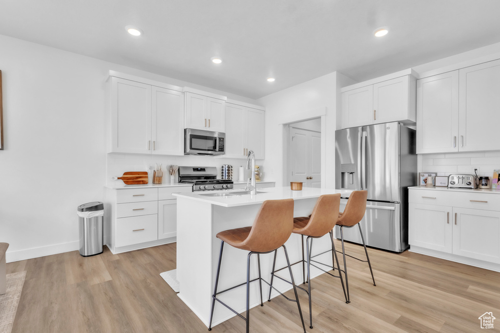 Kitchen with stainless steel appliances, a breakfast bar, light countertops, light wood-style flooring, and a kitchen island with sink
