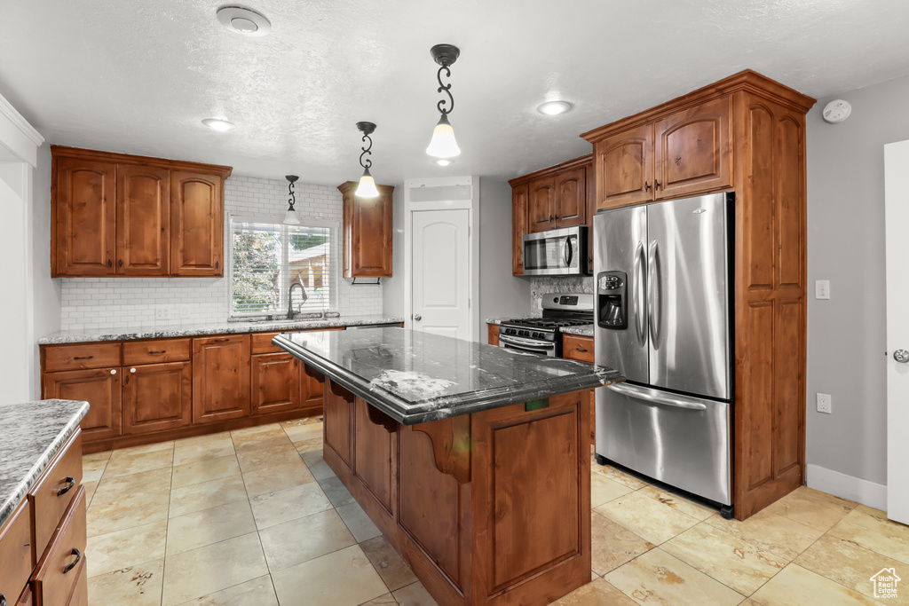 Kitchen featuring stainless steel appliances, backsplash, a center island, dark stone countertops, and hanging light fixtures