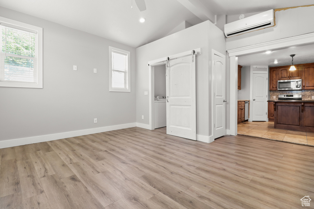 Unfurnished living room featuring a wall unit AC, a barn door, ceiling fan, light wood finished floors, and recessed lighting