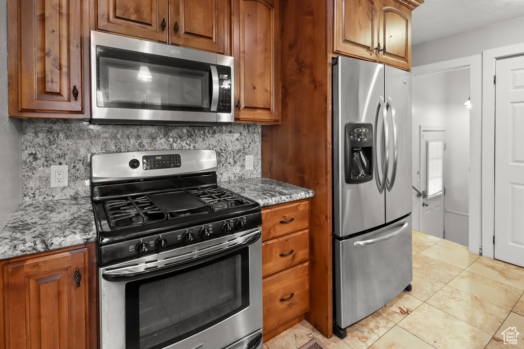 Kitchen featuring appliances with stainless steel finishes, brown cabinetry, backsplash, and light stone counters