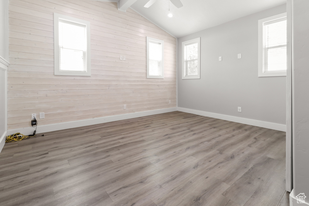 Unfurnished room with wood walls, a ceiling fan, healthy amount of natural light, and wood finished floors