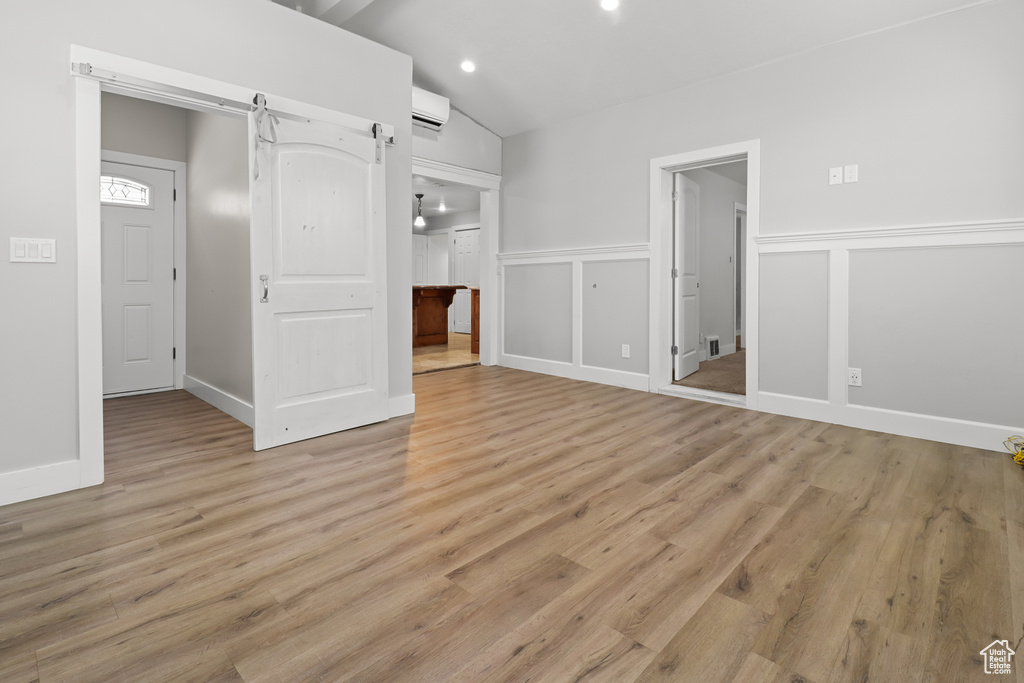 Unfurnished bedroom featuring light wood-style flooring, vaulted ceiling, a decorative wall, ensuite bathroom, and recessed lighting