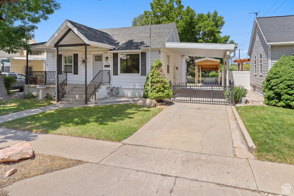 View of front facade with concrete driveway, a carport, roof with shingles, and a gate