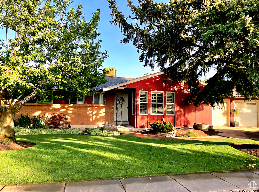 View of front of house with brick siding, a front lawn, roof with shingles, and a garage