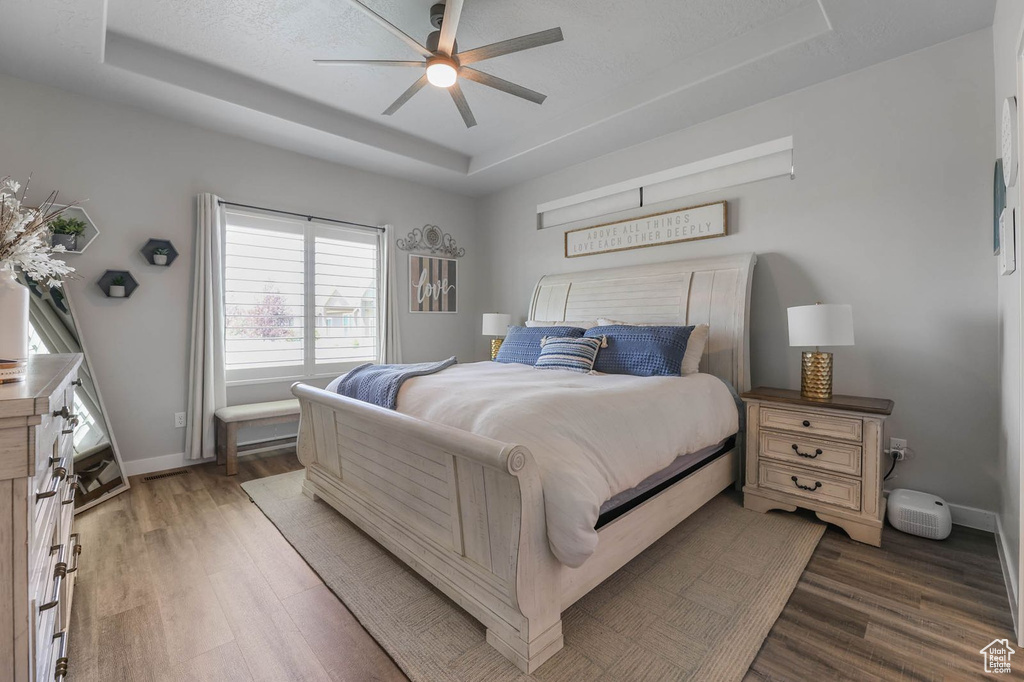 Bedroom with a raised ceiling, wood finished floors, and a ceiling fan