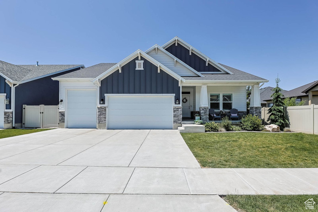 Craftsman-style house featuring board and batten siding, an attached garage, a porch, driveway, and stone siding