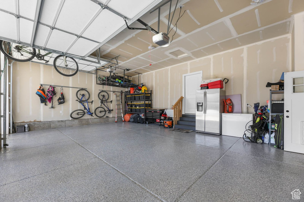 Garage with stainless steel fridge with ice dispenser and a garage door opener