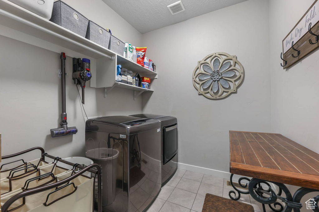 Laundry area featuring washer and clothes dryer, light tile patterned floors, and a textured ceiling