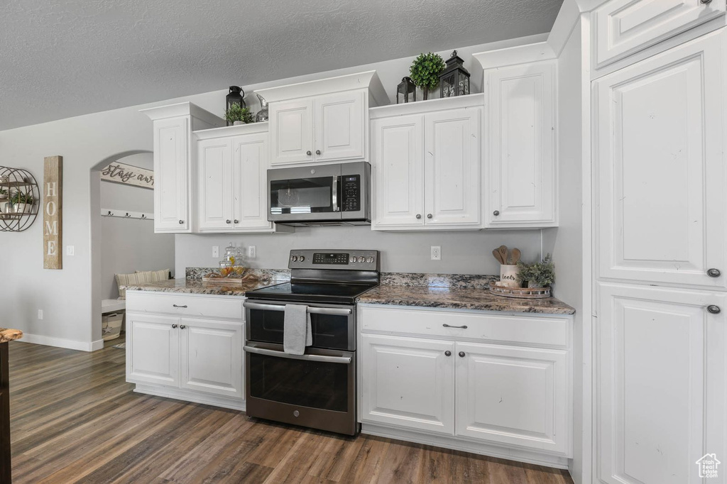 Kitchen featuring appliances with stainless steel finishes, dark wood-style floors, white cabinetry, dark stone counters, and a textured ceiling