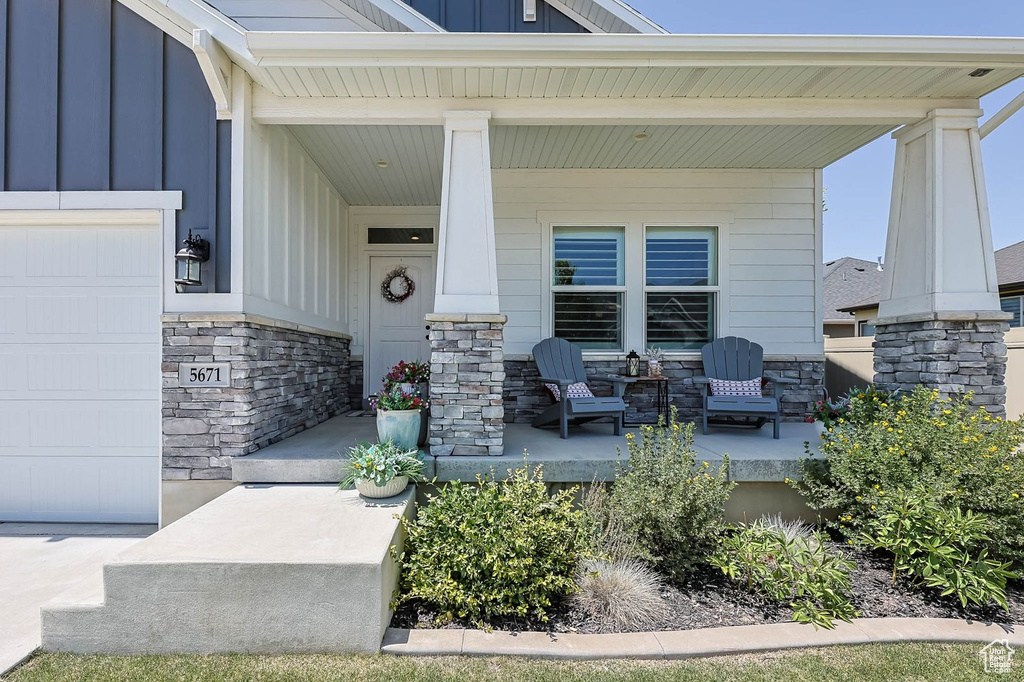 Entrance to property with covered porch, stone siding, board and batten siding, and an attached garage