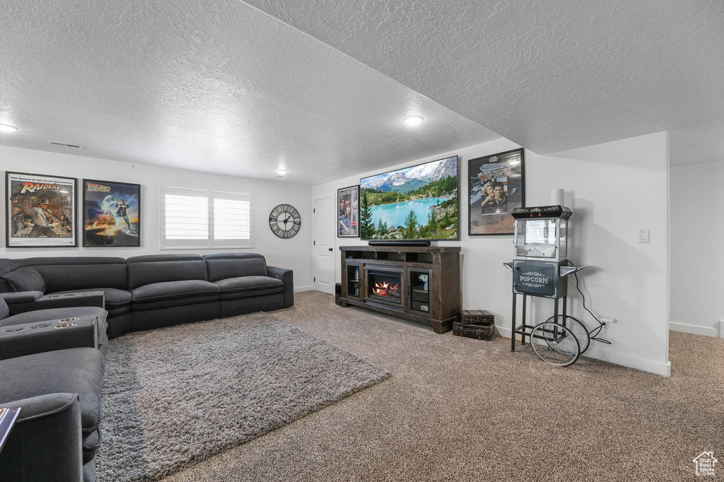 Carpeted living area with a textured ceiling and a warm lit fireplace