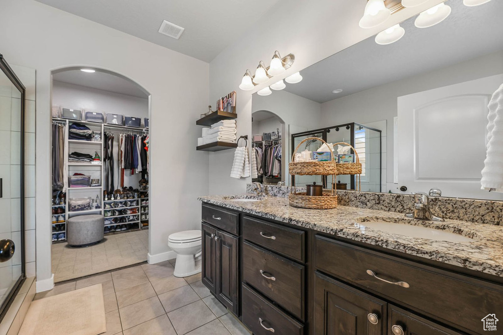 Full bathroom with a walk in closet, double vanity, a shower stall, and tile patterned flooring