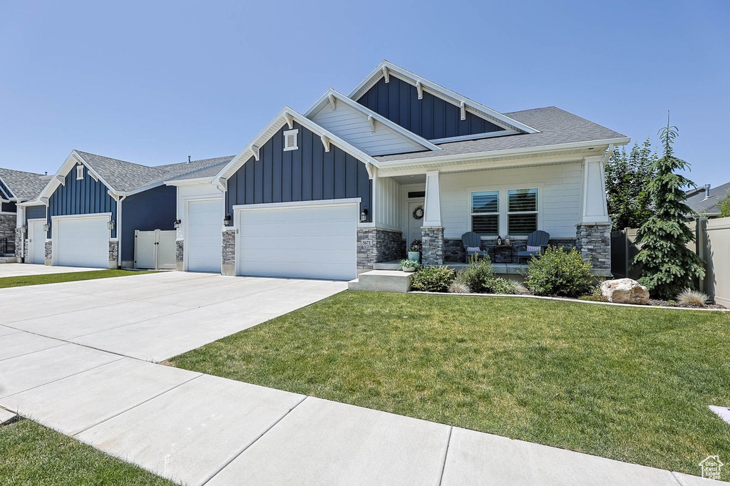 Craftsman-style house with board and batten siding, covered porch, an attached garage, driveway, and stone siding