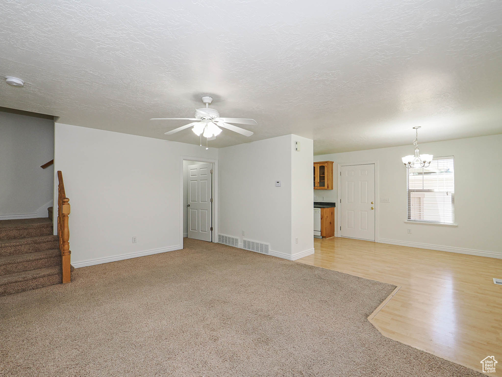 Unfurnished living room featuring a chandelier, stairs, ceiling fan, light wood-style floors, and a textured ceiling
