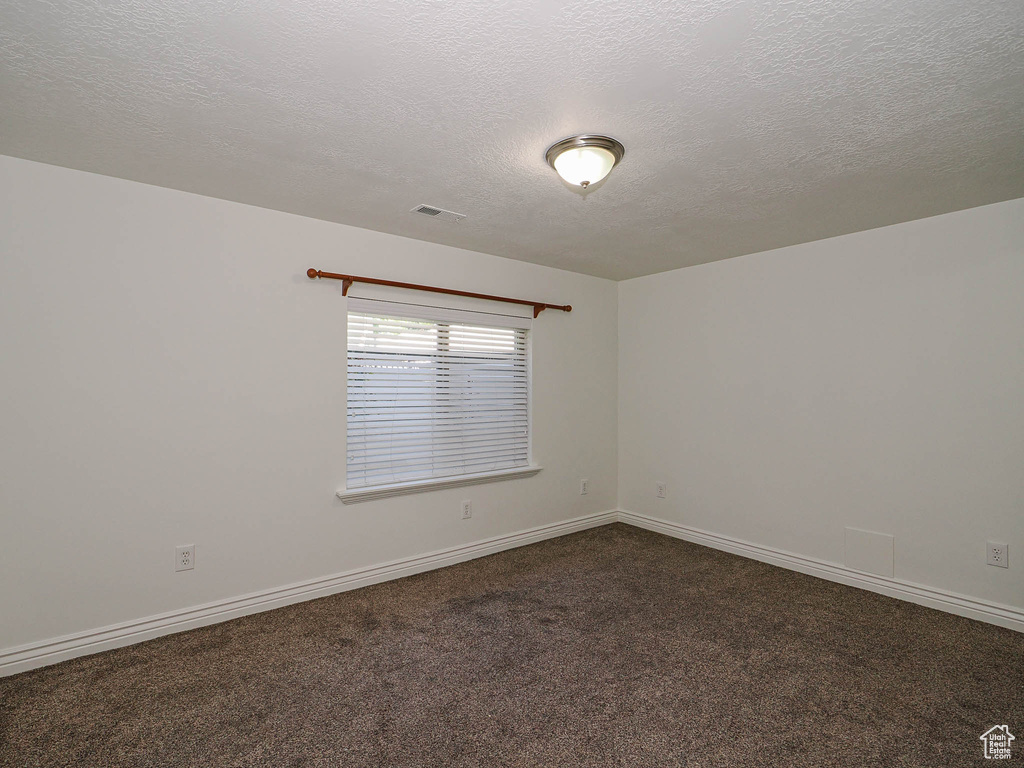 Empty room featuring a textured ceiling and dark colored carpet