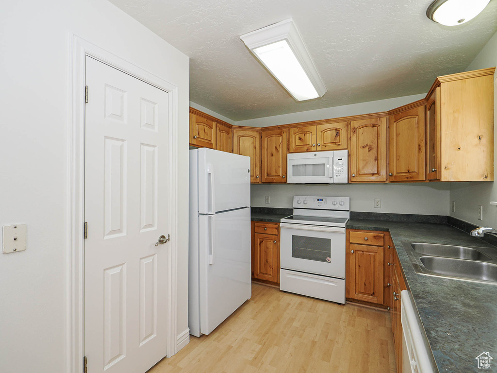 Kitchen with white appliances, dark countertops, brown cabinetry, and a textured ceiling