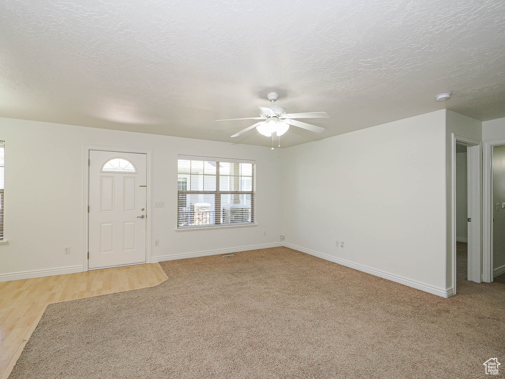Foyer with ceiling fan, a textured ceiling, light colored carpet, and light wood-style flooring