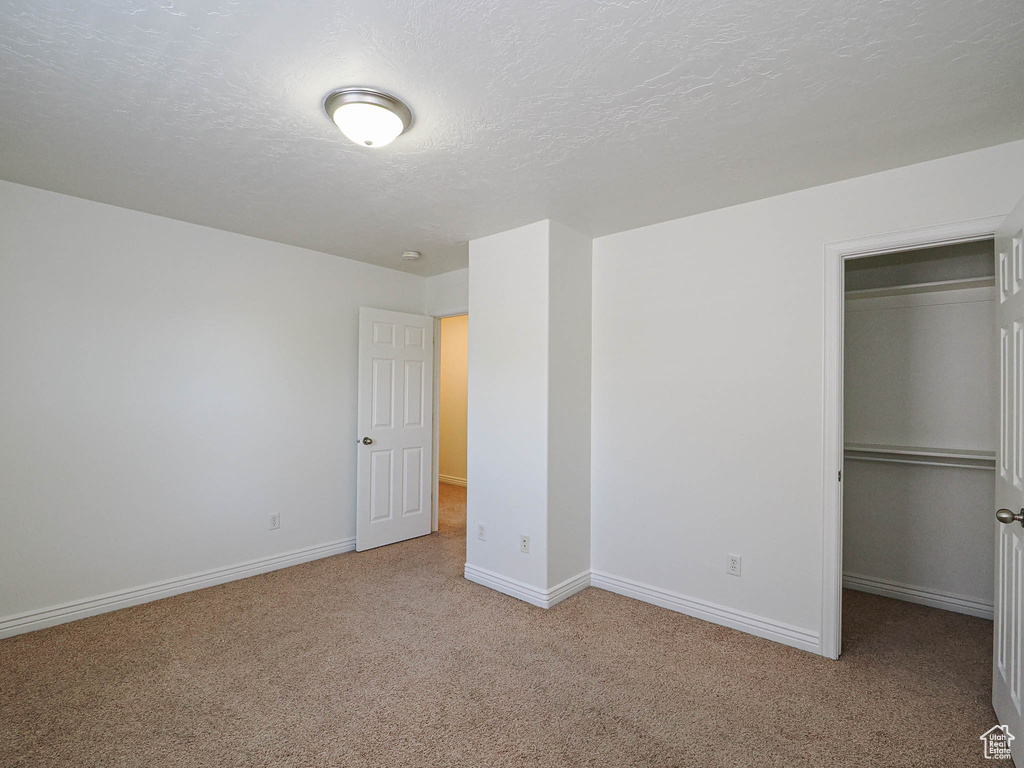 Unfurnished bedroom featuring carpet, a closet, a walk in closet, and a textured ceiling