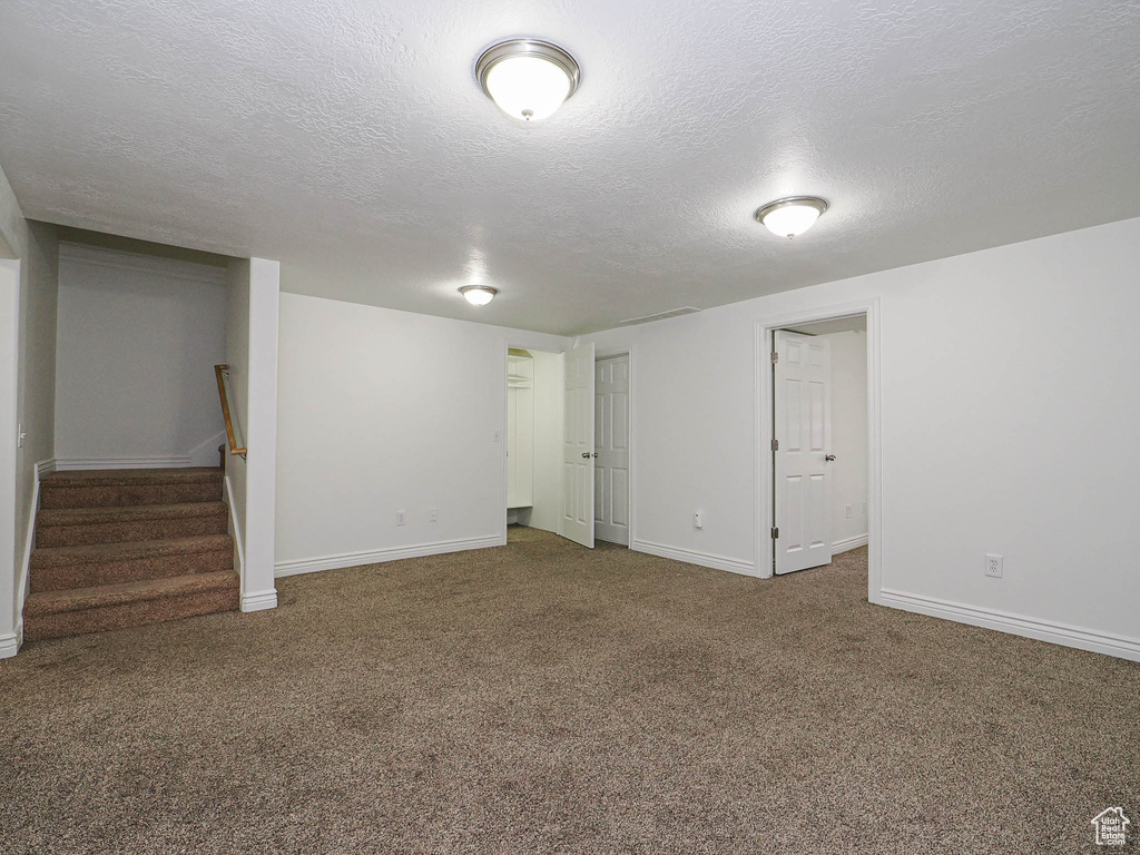 Below grade area with a textured ceiling, carpet, and stairs