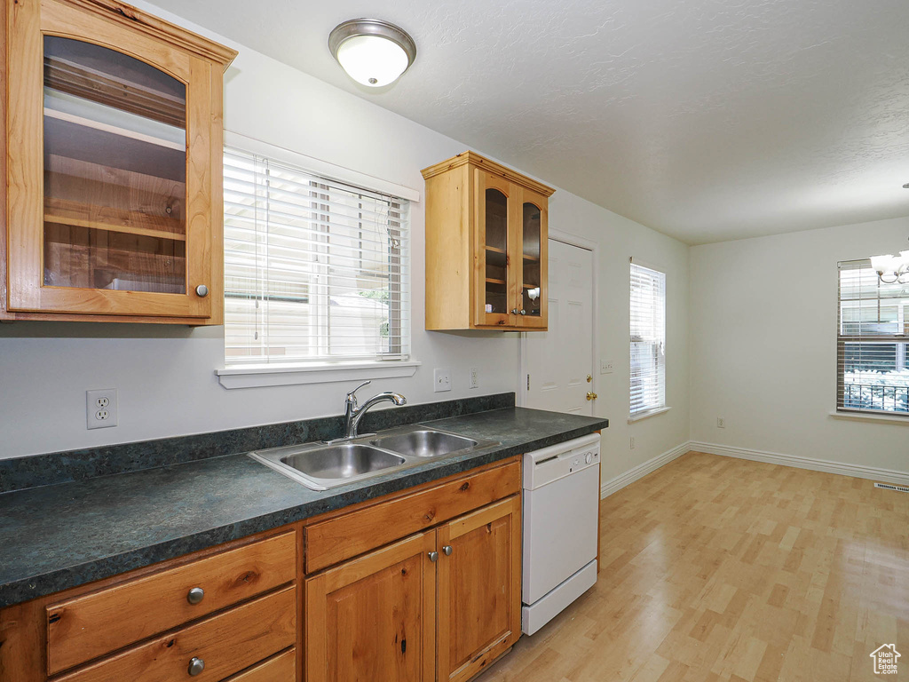 Kitchen with white dishwasher, glass insert cabinets, light wood finished floors, brown cabinetry, and dark countertops