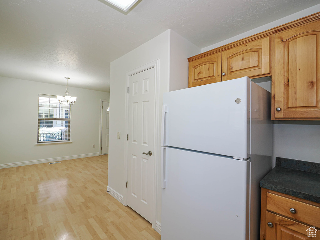 Kitchen featuring freestanding refrigerator, a chandelier, light wood-type flooring, dark countertops, and brown cabinets